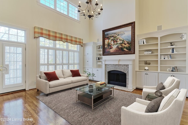 living room with a towering ceiling, a brick fireplace, light wood-type flooring, and a healthy amount of sunlight