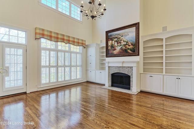 unfurnished living room featuring a towering ceiling, a brick fireplace, a chandelier, and hardwood / wood-style floors