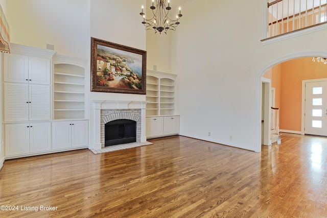 unfurnished living room featuring a high ceiling, an inviting chandelier, built in features, and a fireplace