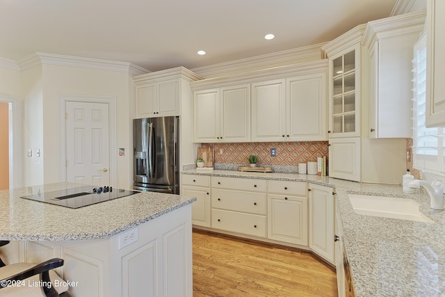 kitchen with a breakfast bar area, light stone countertops, stainless steel fridge, black electric cooktop, and sink