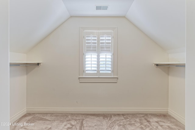 walk in closet with light colored carpet and vaulted ceiling