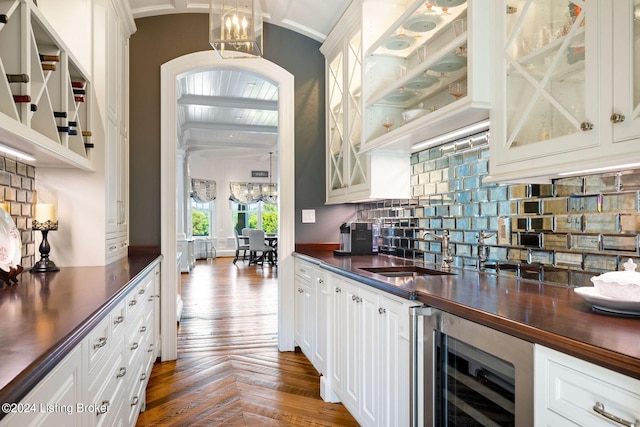 bar with dark parquet flooring, wine cooler, white cabinetry, and sink