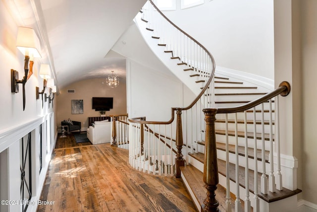 stairs with hardwood / wood-style flooring, lofted ceiling, and a chandelier