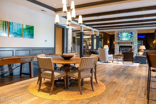 dining room featuring beam ceiling, an inviting chandelier, light hardwood / wood-style floors, a fireplace, and ornamental molding