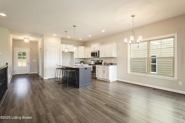 kitchen with appliances with stainless steel finishes, a center island with sink, white cabinetry, and decorative light fixtures