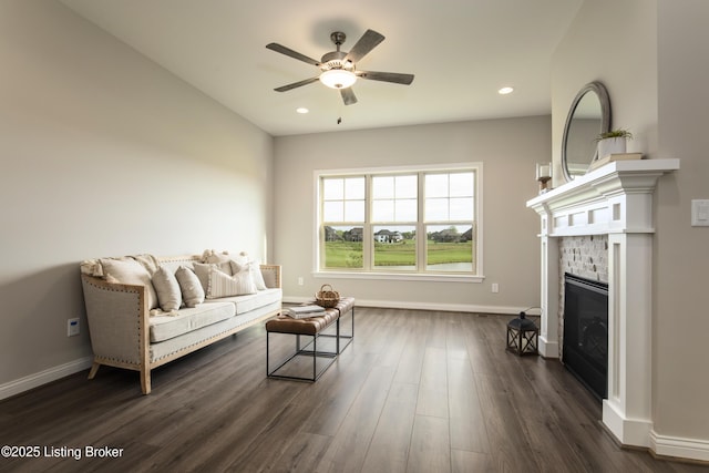 living room featuring ceiling fan, a fireplace, and dark wood-type flooring