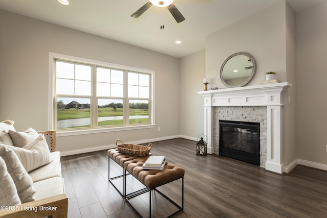 living room with ceiling fan, a stone fireplace, and dark wood-type flooring