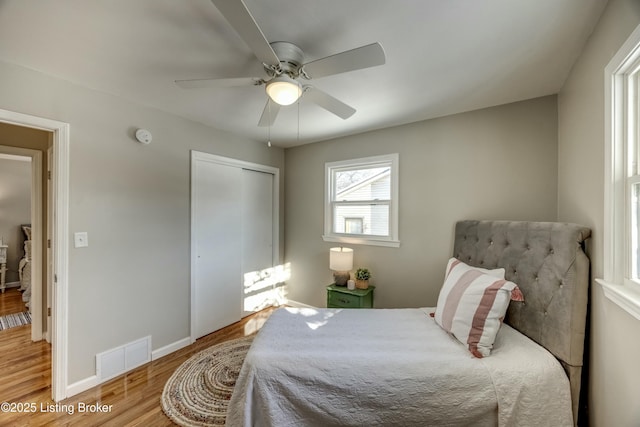 bedroom with ceiling fan, wood finished floors, visible vents, baseboards, and a closet