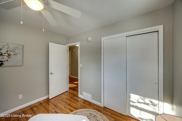 bedroom featuring ceiling fan, wood finished floors, visible vents, baseboards, and a closet