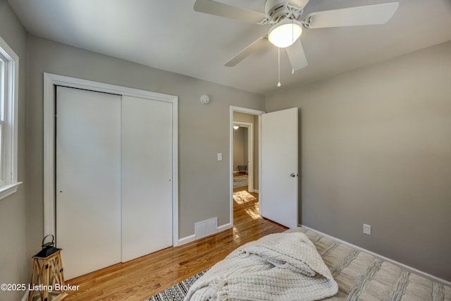 bedroom with a closet, visible vents, ceiling fan, wood finished floors, and baseboards