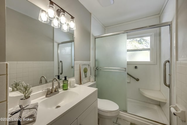 bathroom with toilet, a wainscoted wall, vanity, a shower stall, and tile walls