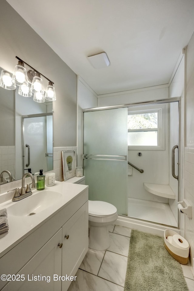 bathroom featuring marble finish floor, tile walls, toilet, a shower stall, and vanity