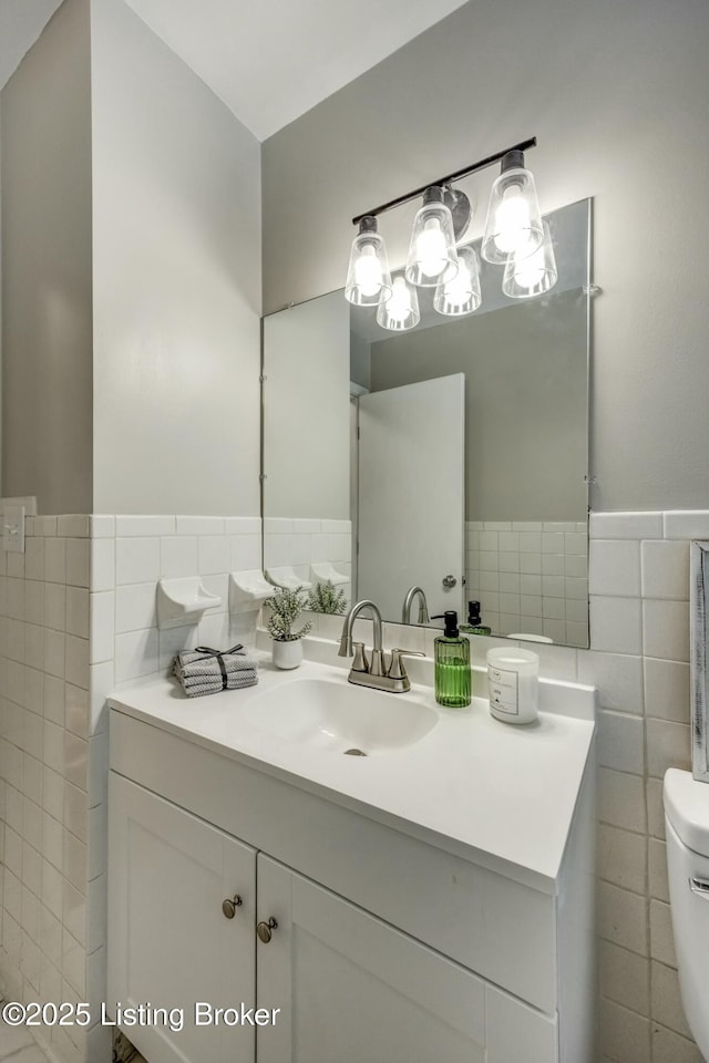 bathroom with toilet, wainscoting, vanity, and tile walls