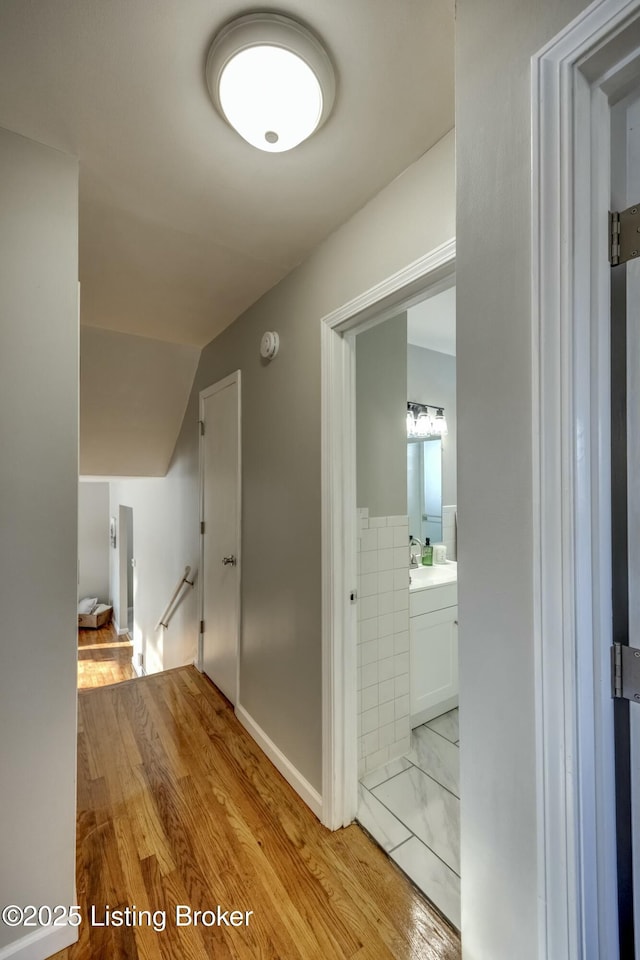 hallway with a sink, light wood finished floors, and an upstairs landing