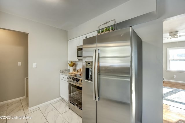 kitchen with marble finish floor, backsplash, appliances with stainless steel finishes, white cabinetry, and baseboards