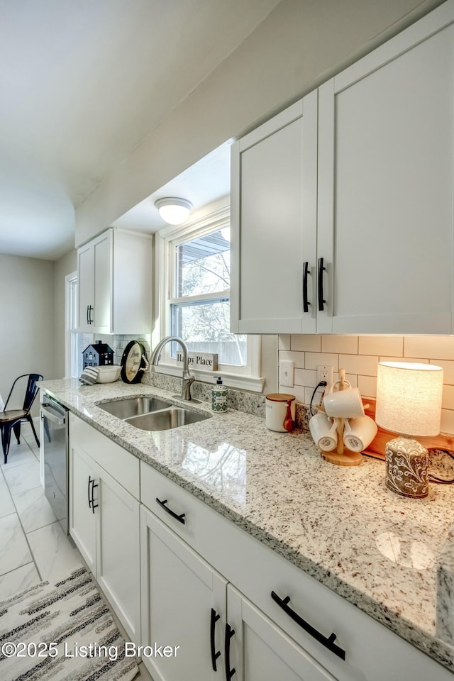 kitchen with marble finish floor, tasteful backsplash, stainless steel dishwasher, white cabinetry, and a sink