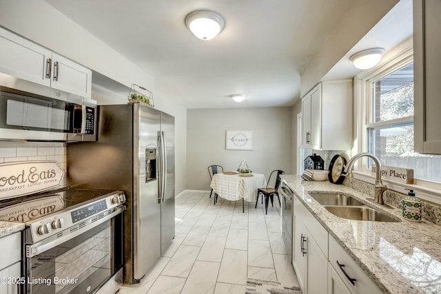 kitchen featuring appliances with stainless steel finishes, a sink, white cabinets, and tasteful backsplash