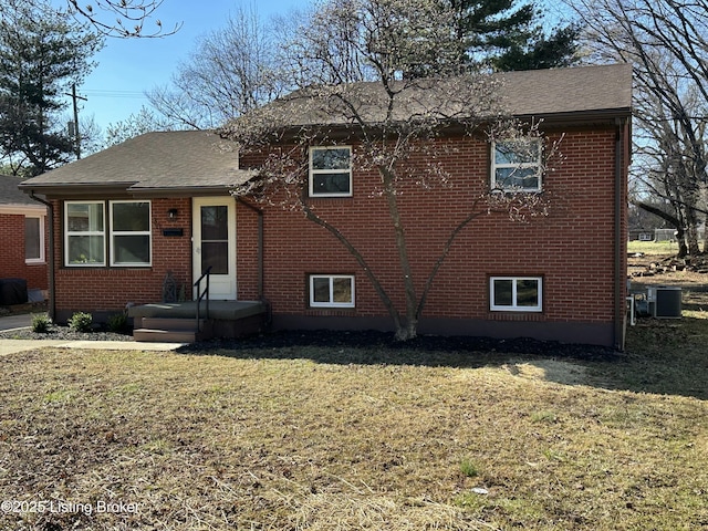 view of front facade with central air condition unit, brick siding, and a front yard