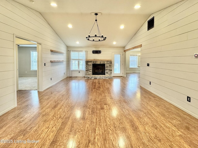 unfurnished living room with a stone fireplace, wooden walls, vaulted ceiling, and light wood-type flooring