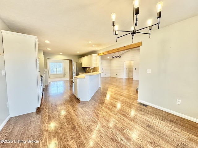 kitchen featuring stainless steel fridge, decorative light fixtures, a center island with sink, light hardwood / wood-style flooring, and white cabinetry