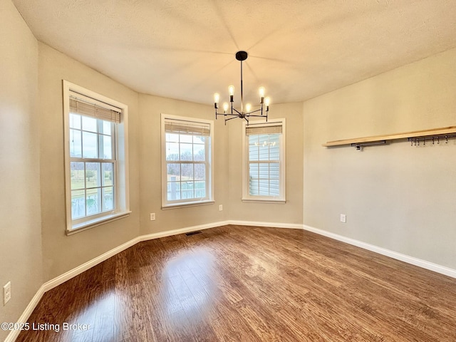 unfurnished dining area featuring hardwood / wood-style floors, a textured ceiling, and a notable chandelier