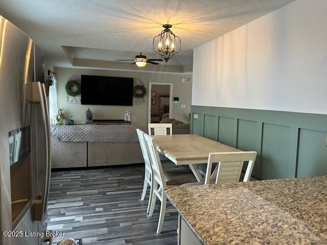 dining area with dark hardwood / wood-style flooring, ceiling fan with notable chandelier, and a tray ceiling