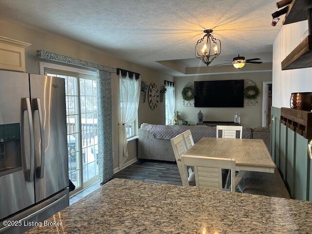 kitchen with stainless steel fridge, ceiling fan with notable chandelier, light stone counters, and dark hardwood / wood-style flooring