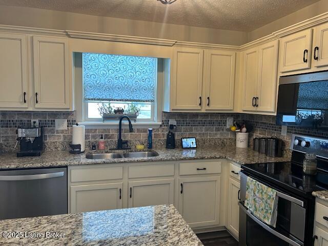 kitchen featuring white cabinetry, sink, light stone countertops, tasteful backsplash, and appliances with stainless steel finishes