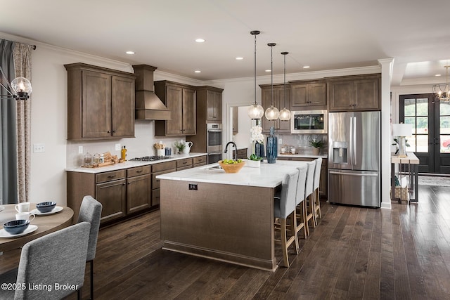 kitchen with dark wood-type flooring, stainless steel appliances, premium range hood, pendant lighting, and a center island with sink