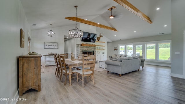 dining area with high vaulted ceiling, light hardwood / wood-style floors, beamed ceiling, and a stone fireplace