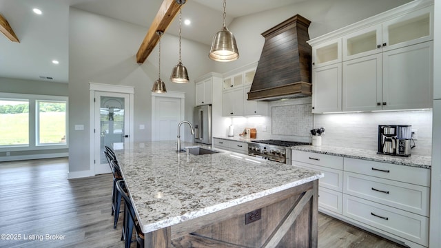 kitchen with hanging light fixtures, an island with sink, beamed ceiling, sink, and white cabinetry