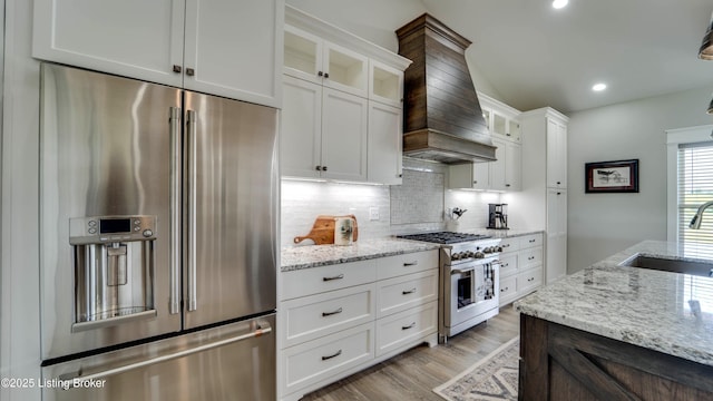 kitchen featuring custom range hood, high quality appliances, light stone counters, sink, and white cabinetry