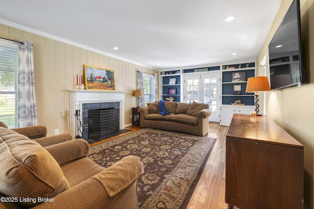 living room featuring hardwood / wood-style flooring, built in features, crown molding, and a tile fireplace