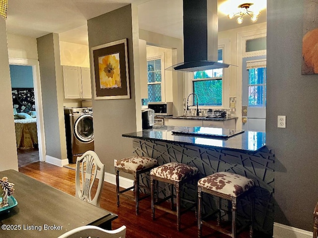 kitchen featuring island exhaust hood, dark hardwood / wood-style flooring, sink, washer / dryer, and white cabinetry