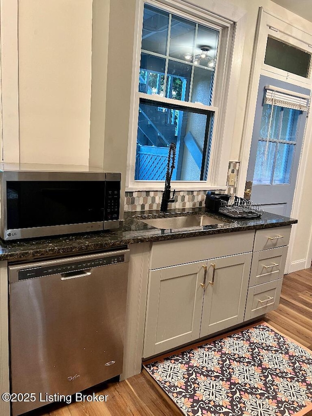 kitchen with appliances with stainless steel finishes, gray cabinetry, sink, dark stone countertops, and light hardwood / wood-style floors