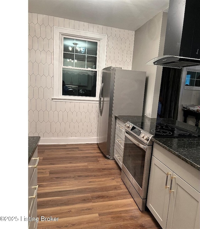 kitchen with wall chimney exhaust hood, dark hardwood / wood-style floors, dark stone countertops, appliances with stainless steel finishes, and white cabinetry