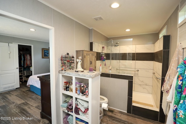 bathroom featuring a tile shower, hardwood / wood-style floors, vanity, and toilet