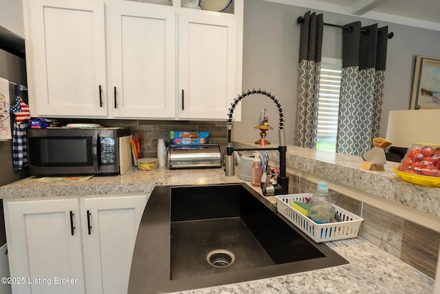 kitchen featuring tasteful backsplash, white cabinetry, sink, and light stone countertops