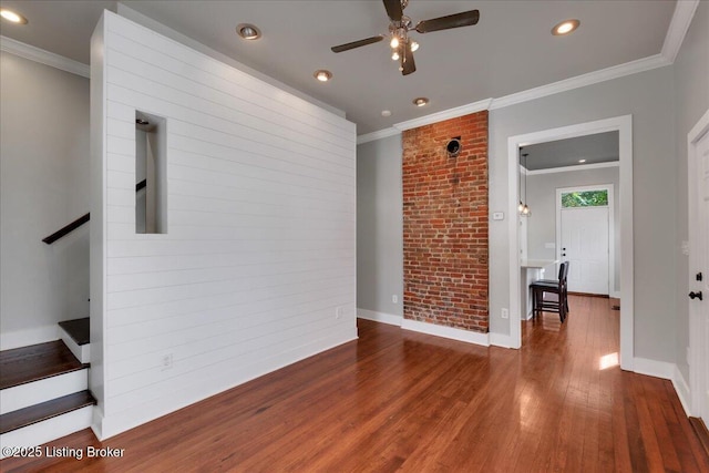 unfurnished room with hardwood / wood-style floors, ceiling fan, crown molding, and brick wall