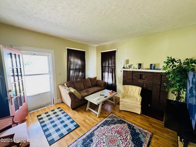 living room with a textured ceiling, hardwood / wood-style flooring, and a brick fireplace