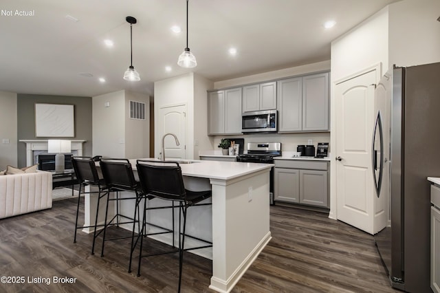 kitchen with sink, dark hardwood / wood-style floors, decorative light fixtures, a center island with sink, and appliances with stainless steel finishes