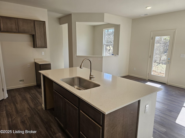 kitchen with dark brown cabinetry, dark wood-style flooring, a sink, baseboards, and light countertops