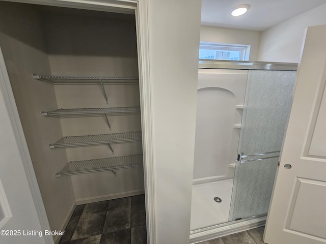 full bath with a walk in closet, a shower stall, and baseboards