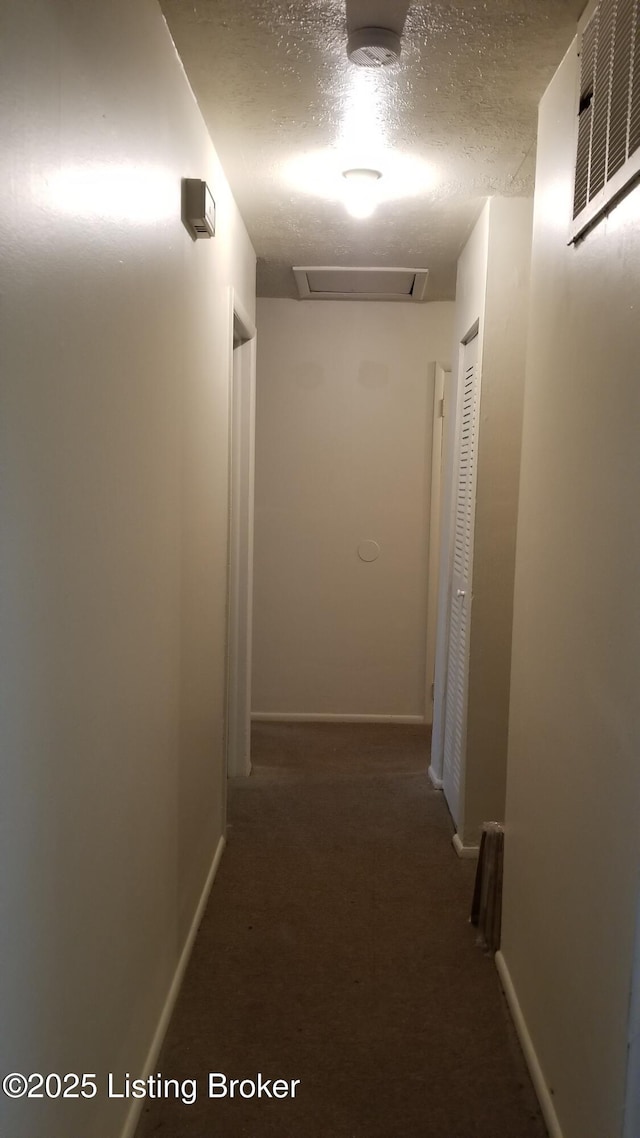 hallway featuring a textured ceiling and dark colored carpet