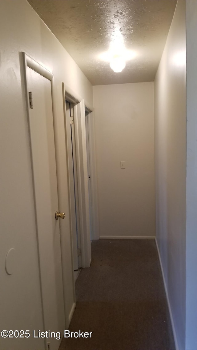 hallway with dark colored carpet and a textured ceiling