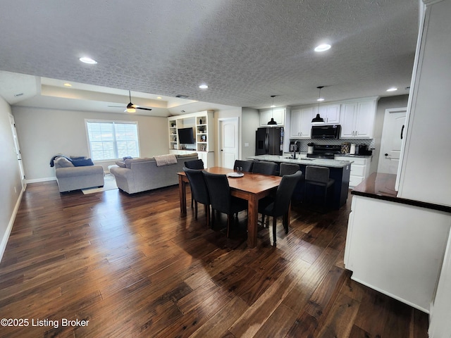 dining area with dark hardwood / wood-style floors, sink, ceiling fan, a tray ceiling, and a textured ceiling