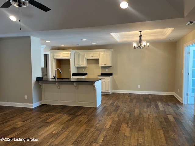 kitchen featuring white cabinetry, sink, a breakfast bar area, dark hardwood / wood-style floors, and a tray ceiling