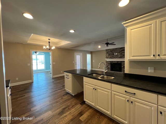 kitchen with a stone fireplace, a raised ceiling, white cabinetry, and sink