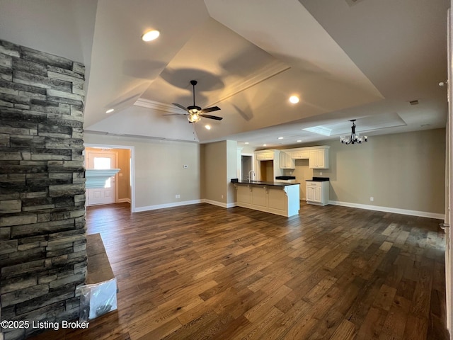 unfurnished living room with ceiling fan with notable chandelier, dark hardwood / wood-style flooring, sink, and a tray ceiling