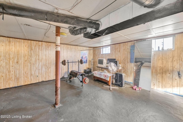 basement featuring a wealth of natural light, a drop ceiling, and wooden walls